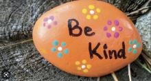 A kindness rock painted orange with flowers and the words, "Be Kind."